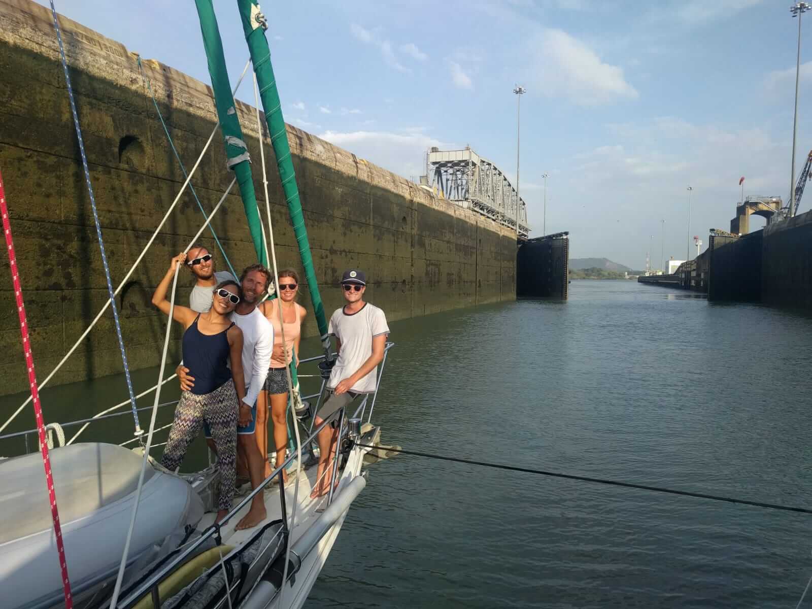 group of friends on the bow of a sailboat during a panama canal crossing in the locks