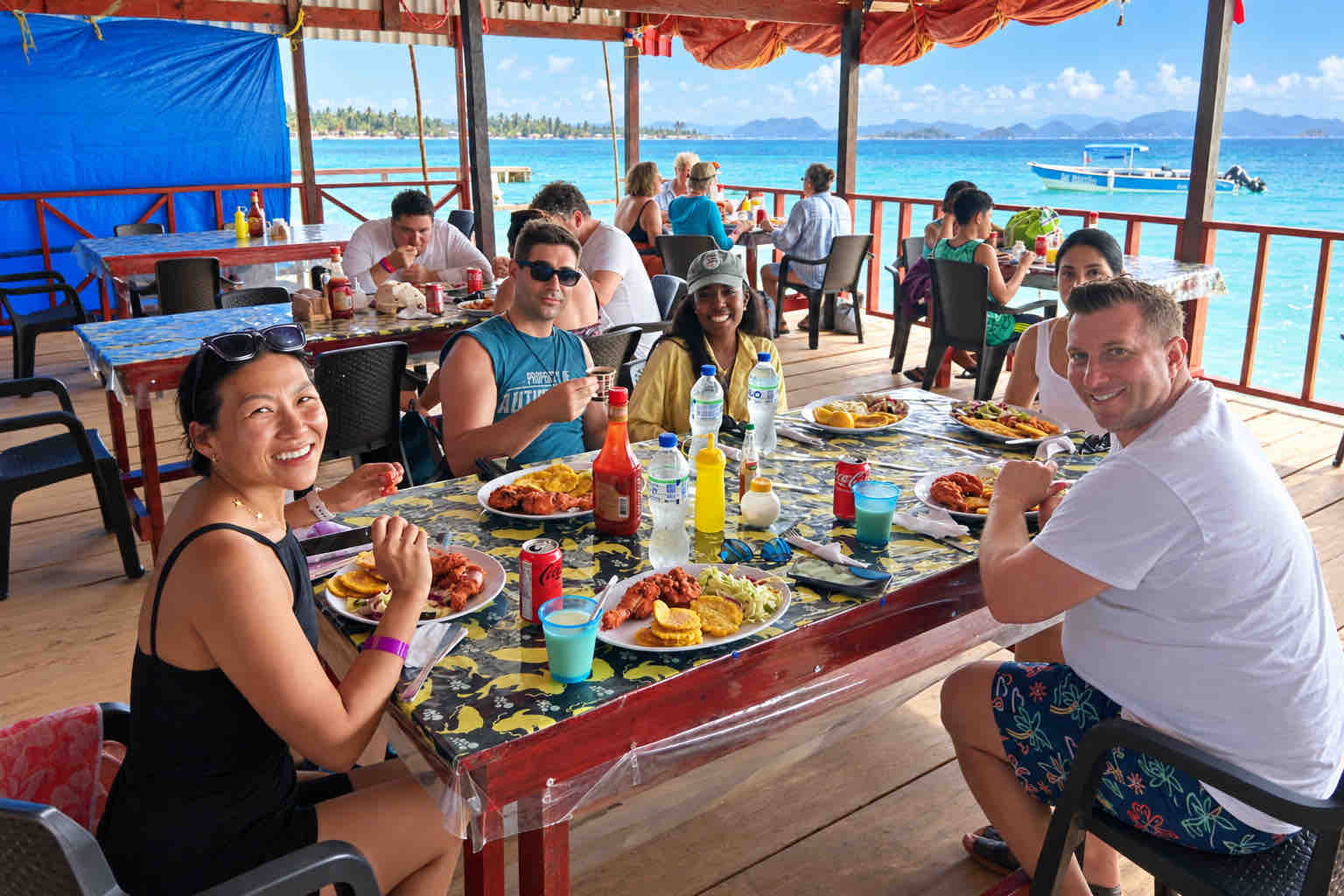 Travelers enjoying lunch around a table in an open-sided island restaurant.