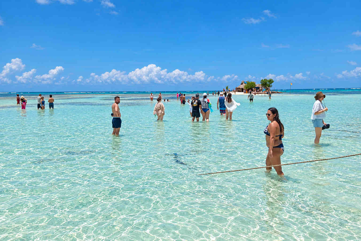 Travelers wading through a broad expanse of clear shallow water in San Blas.