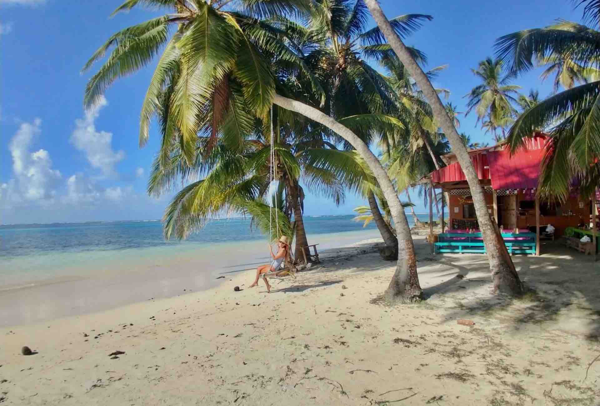San Blas island beach with woman sitting on swing under palm tree