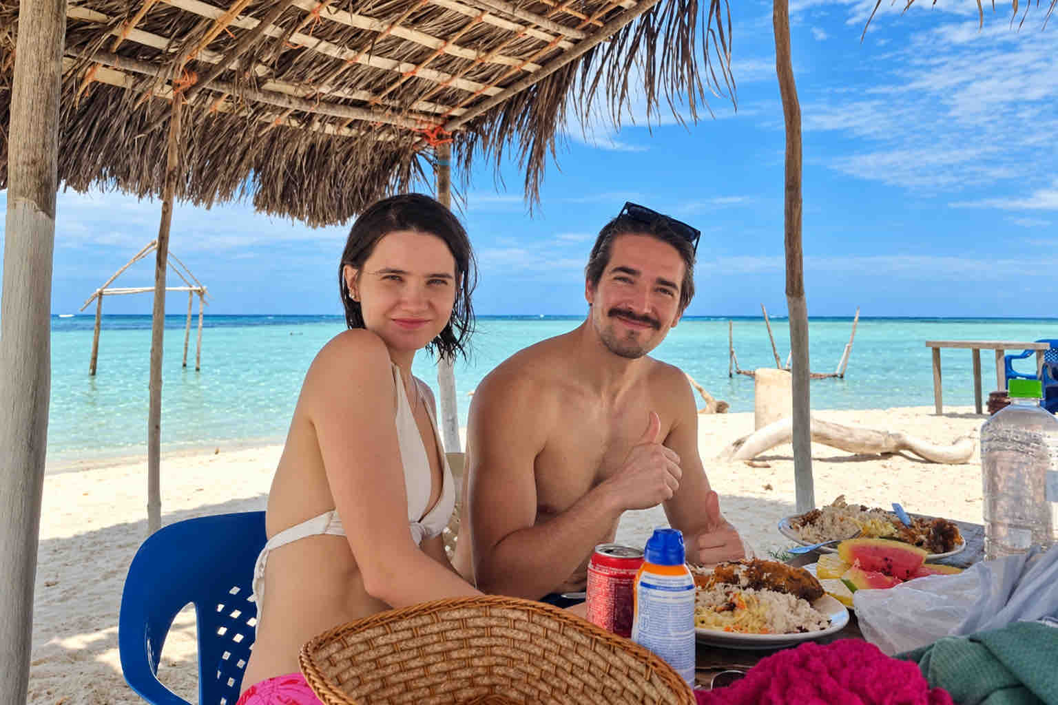 Two guests enjoying lunch beneath a thatched shelter beside the sea on a San Blas Islands tour