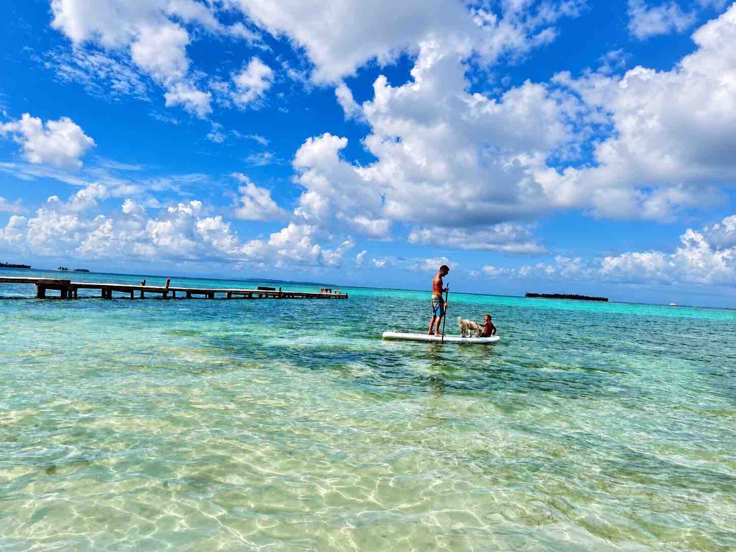 Paddleboarder crossing shallow water beneath a blue sky