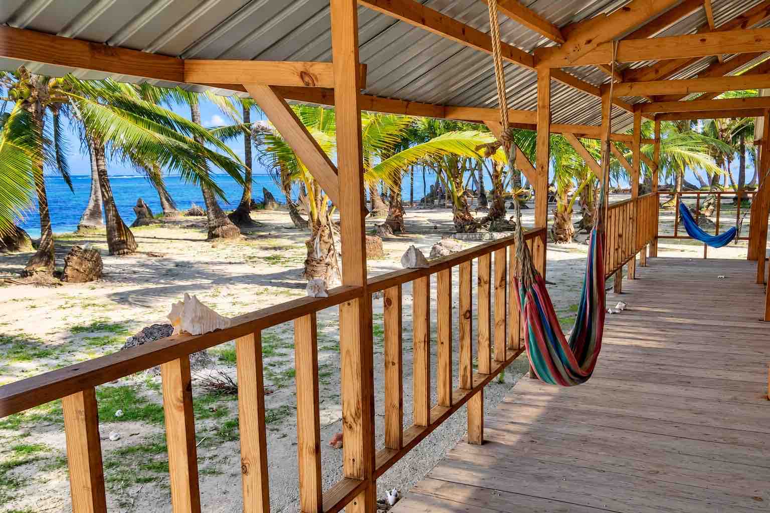 Covered wooden porch with hammocks facing palms and sea
