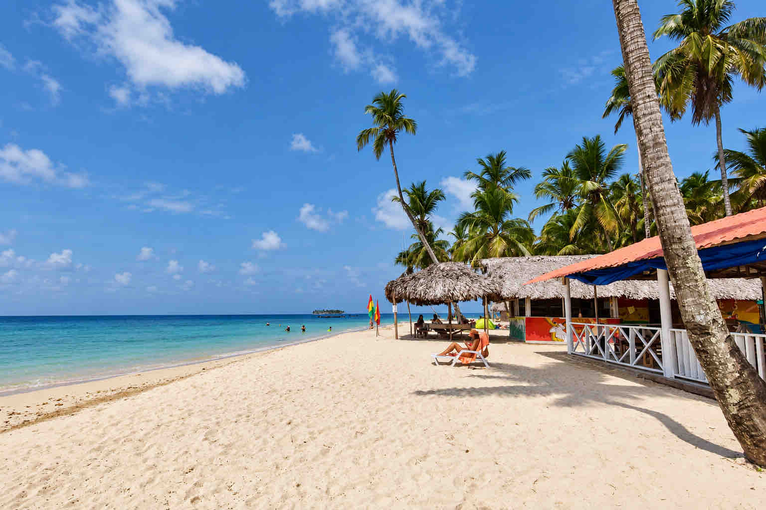 Sandy beach with a thatched palapa, palms and seaside buildings at Isla Asserya on a San Blas beach trip