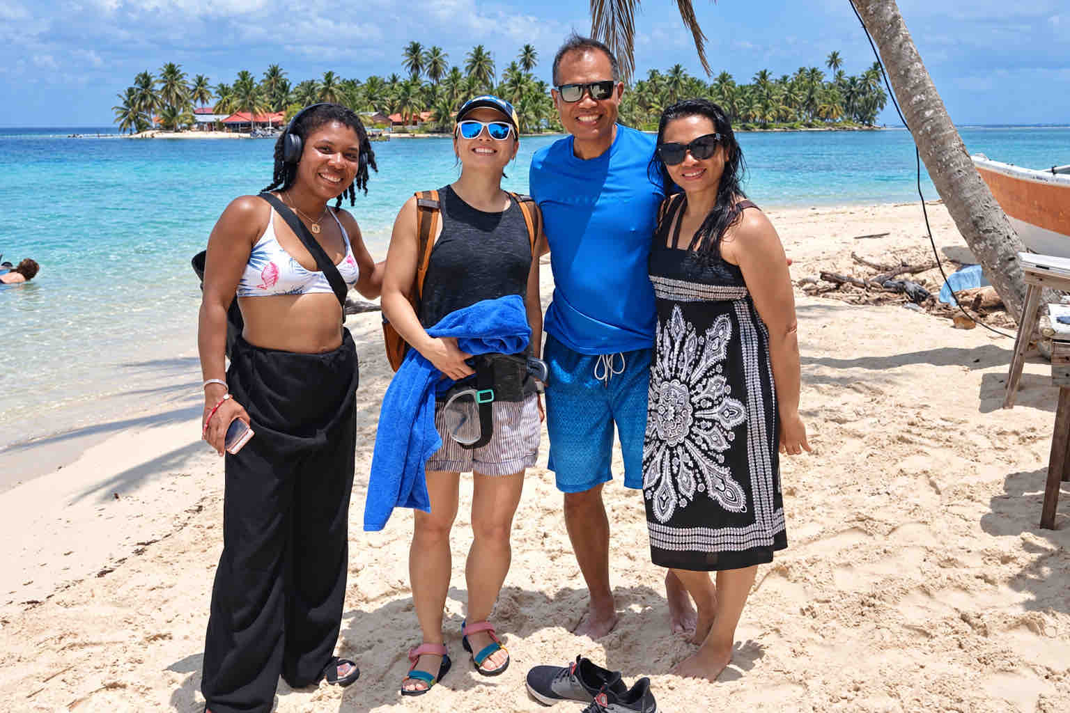 Four travelers posing on a white-sand beach beneath a palm tree during a San Blas beach trip