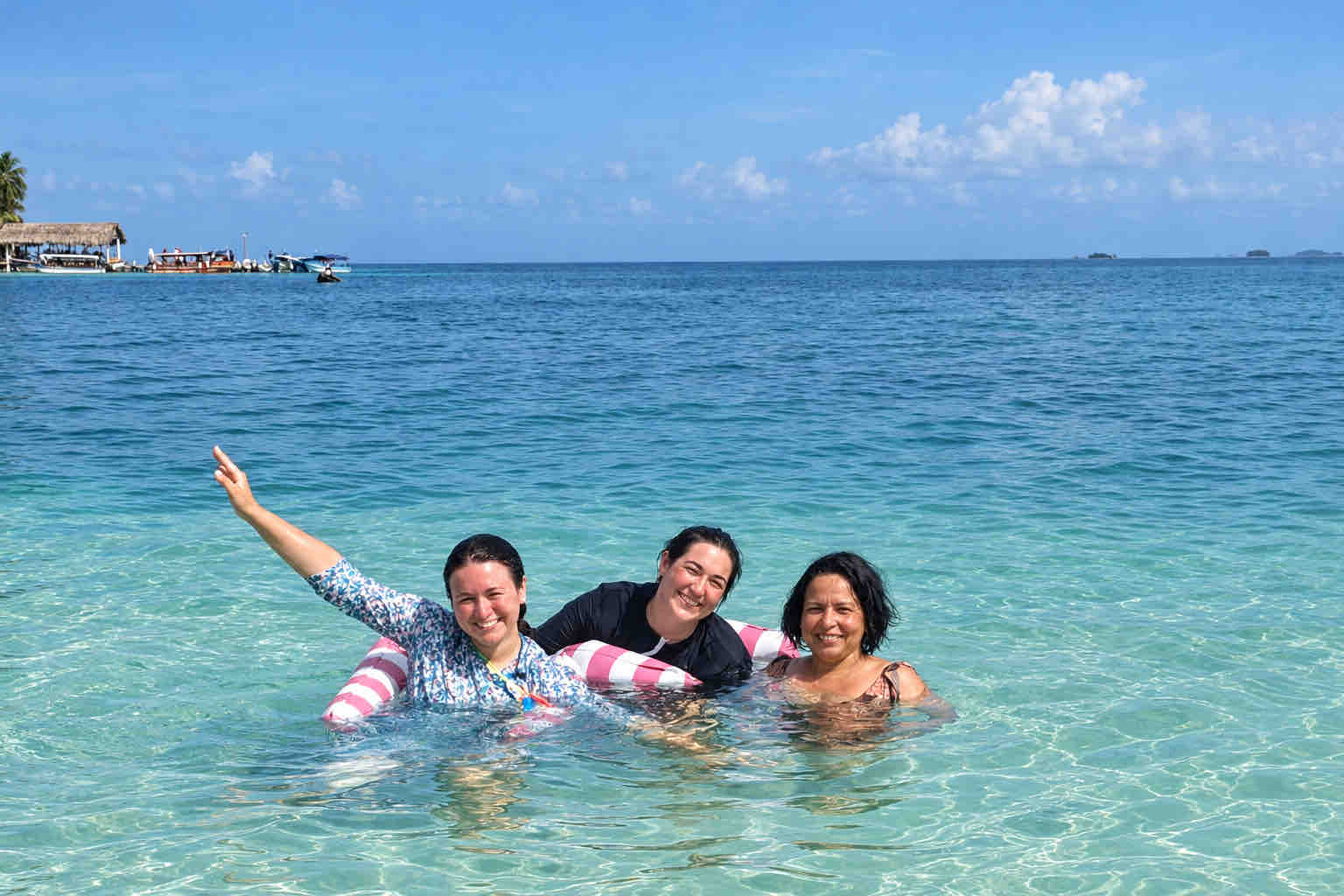 Three women smiling in the sea with a pink and white swim ring during a San Blas beach trip