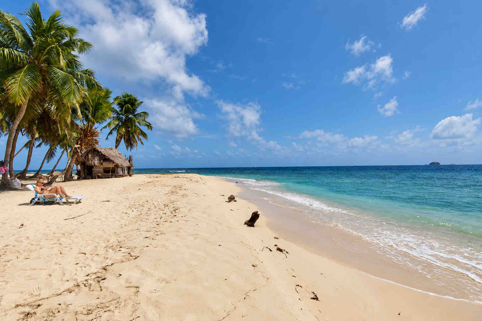 Woman relaxing on a beach lounger beside palms and a thatched hut on a San Blas beach trip