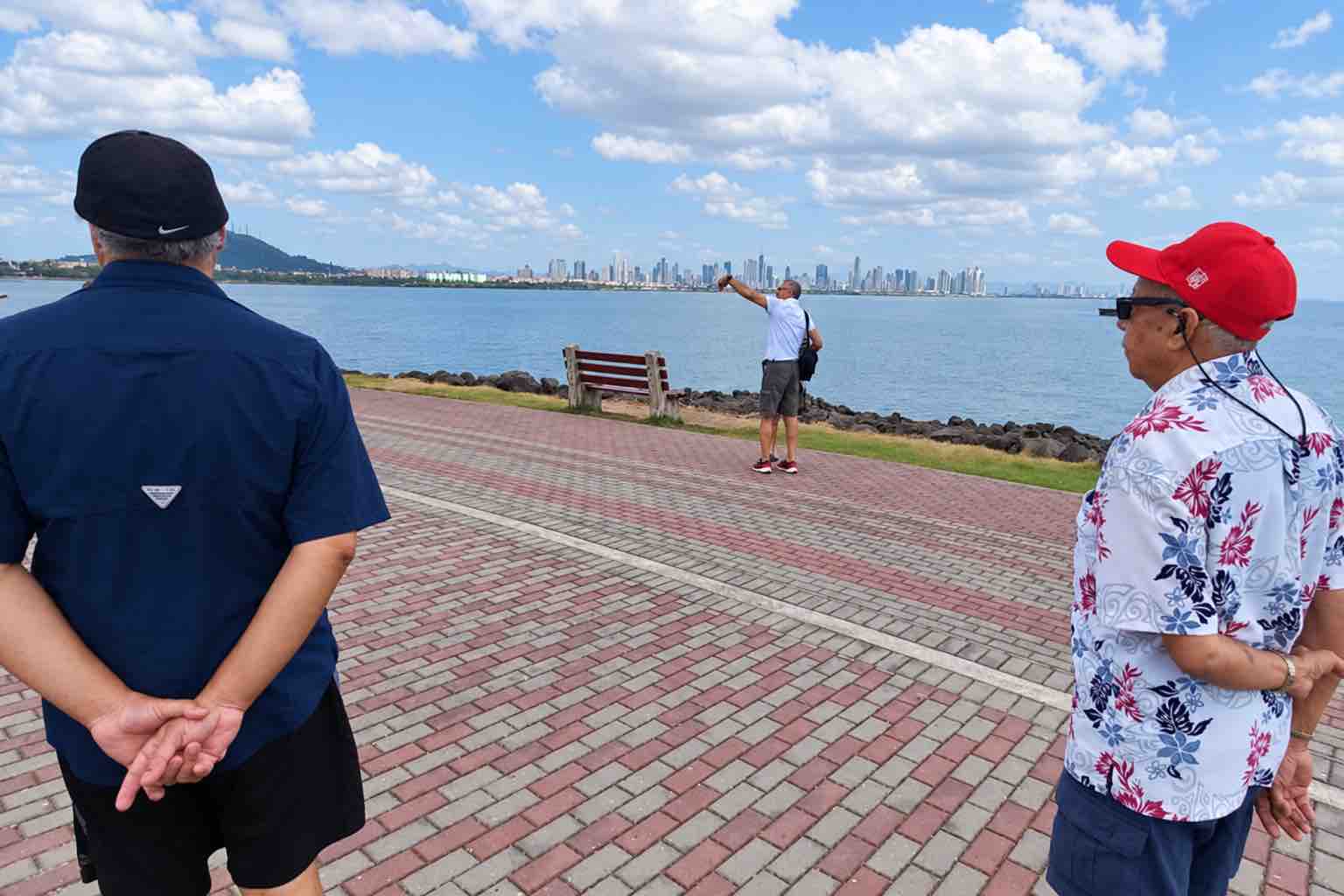 Panama Canal and City Tour guests at Amador Causeway, with a visitor taking a photo and the city skyline across the bay.