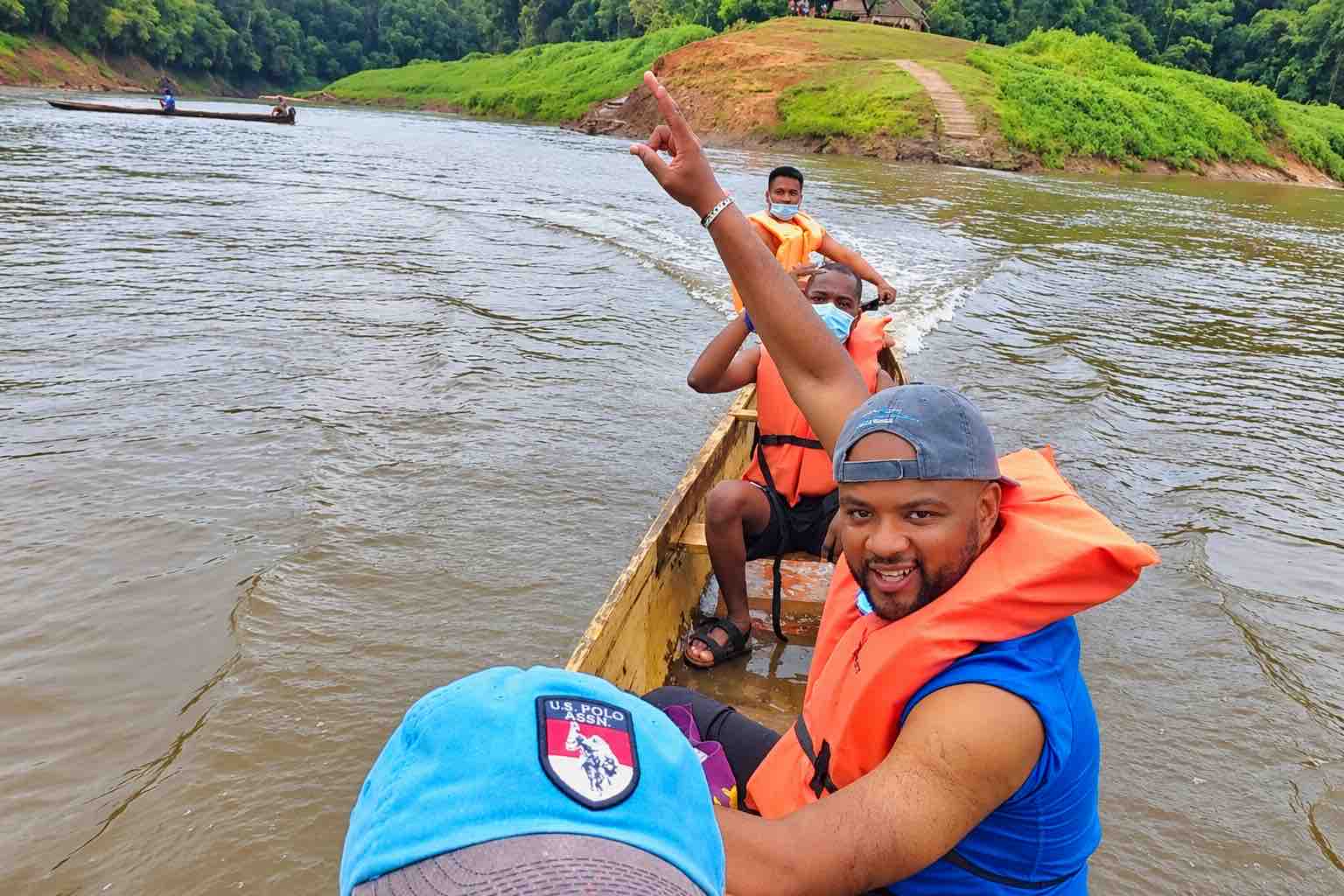 Guests wearing orange life jackets riding in a wooden boat on a river
