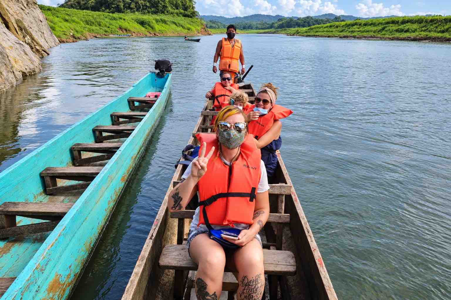 Visitors wearing orange life jackets seated in a wooden canoe beside a turquoise boat