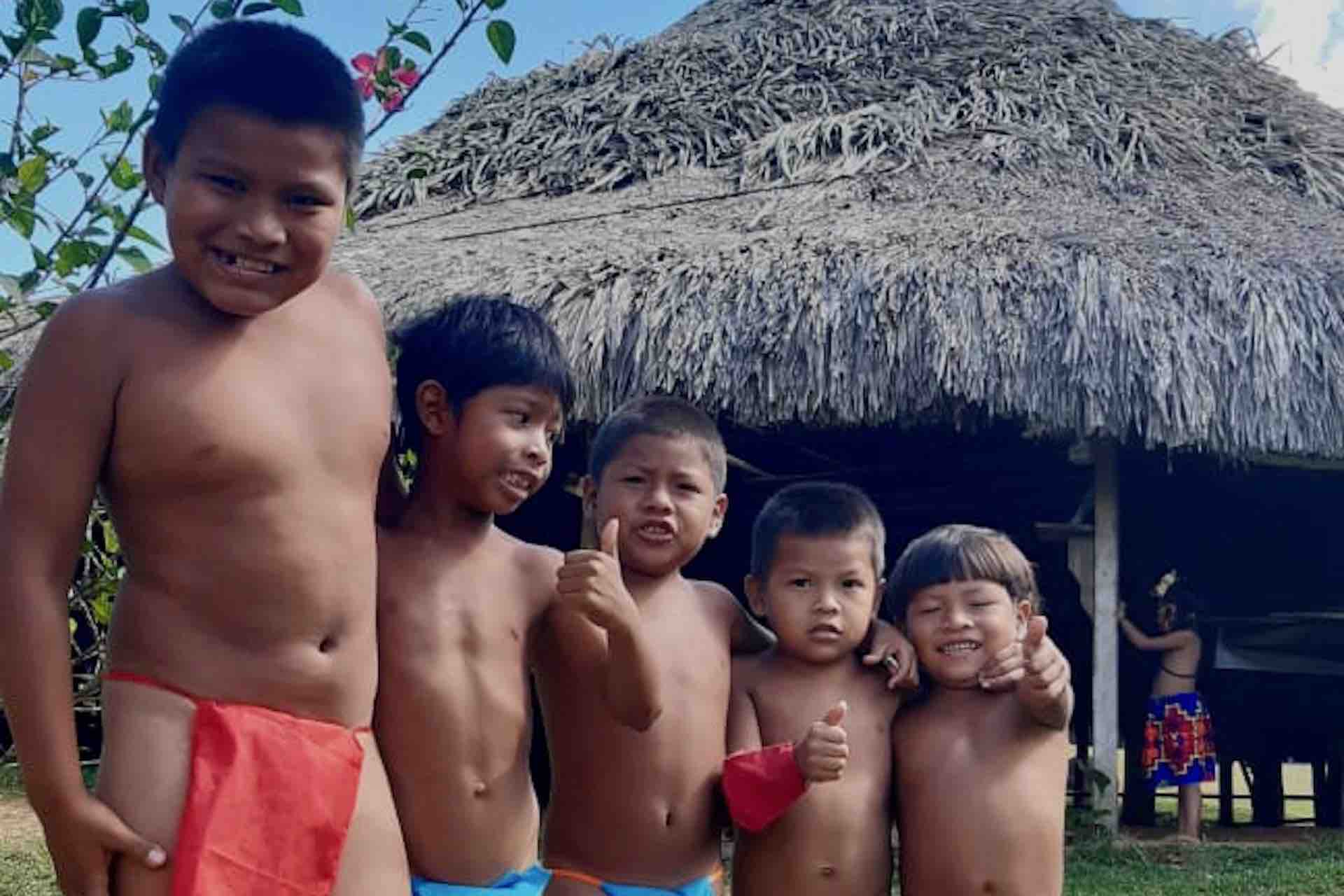 Emberá children posing together in front of a traditional thatched-roof house