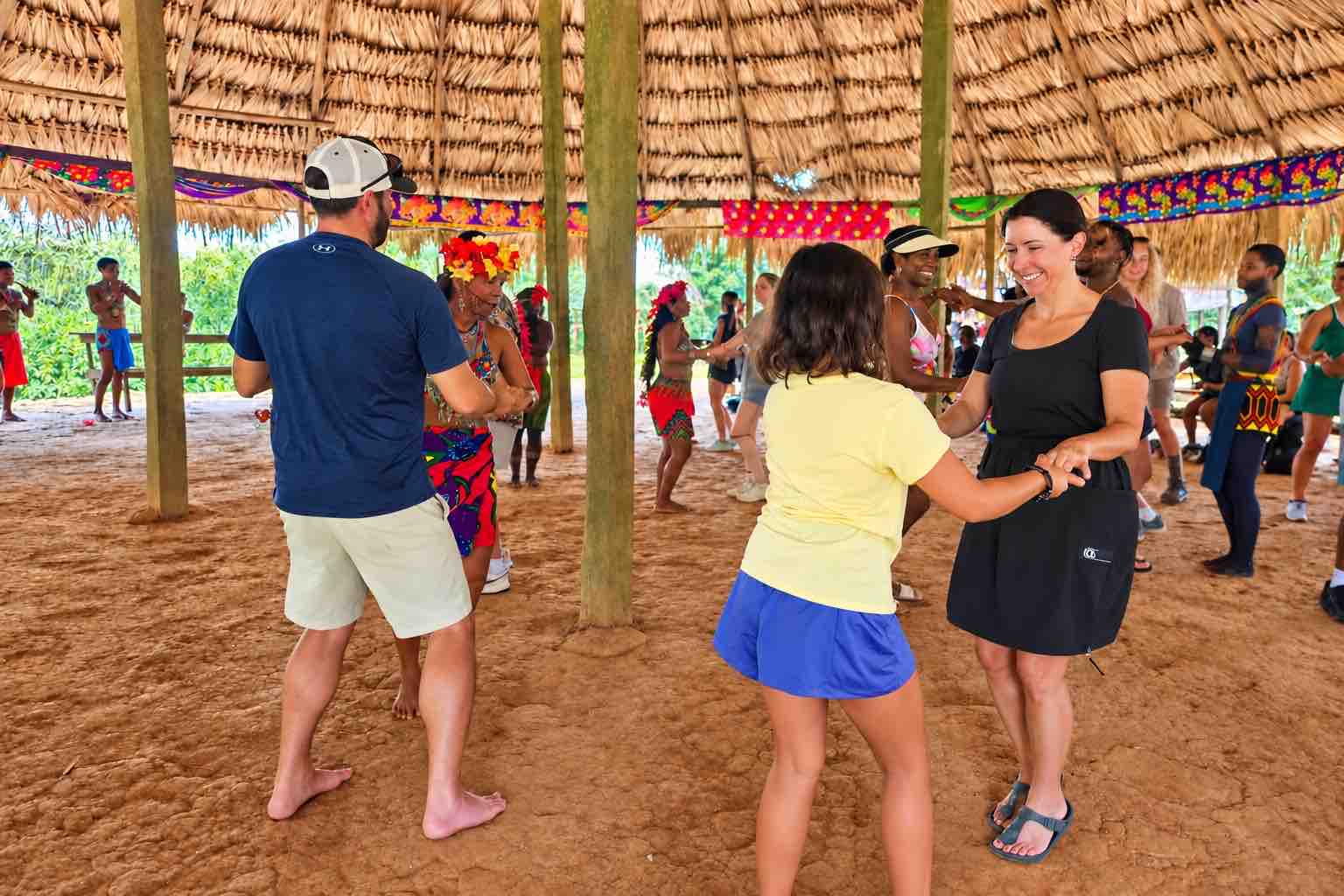 Embera Village Tour – Cultural Dance in Panama Visitors and Emberá hosts dancing together inside a large thatched-roof gathering space