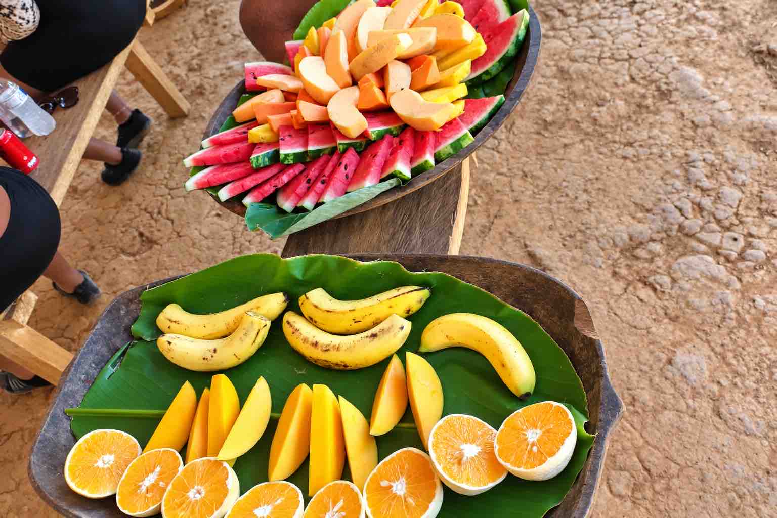 Platters of bananas, citrus, mango and watermelon arranged on green leaves