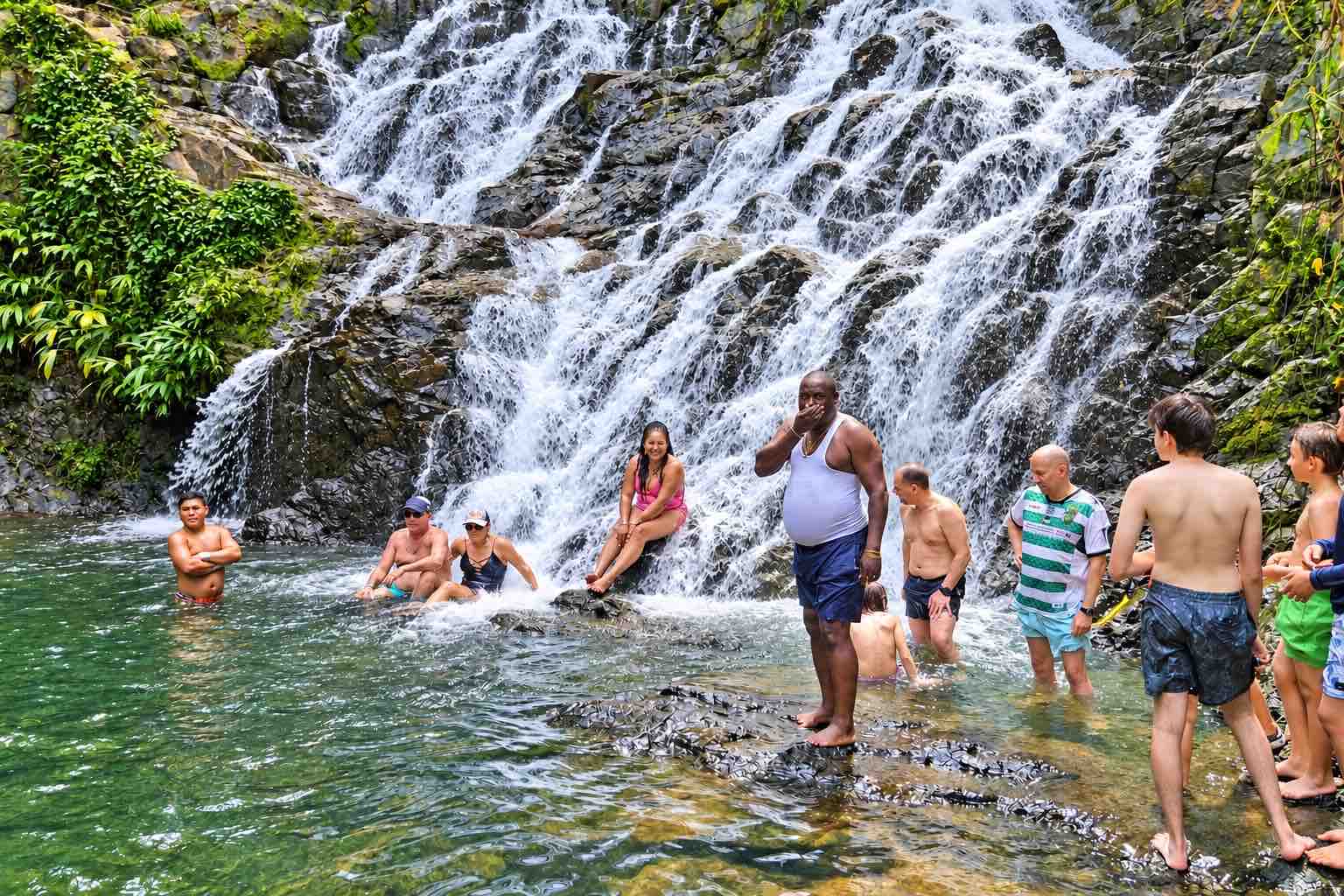 Embera Village Tour – Panama Rainforest Waterfall Visitors swimming and standing on rocks beneath a broad cascading rainforest waterfall