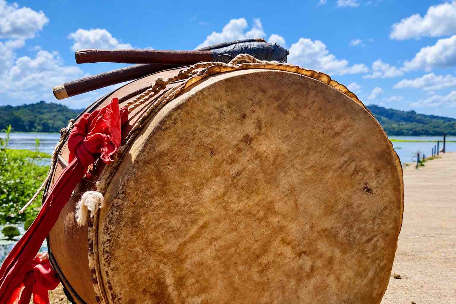 Close-up of a traditional drum and drumsticks with a river and forested hills behind