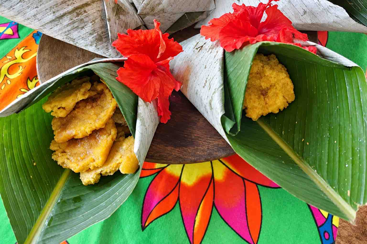 Fried fish and plantain served in folded green leaves decorated with red flowers