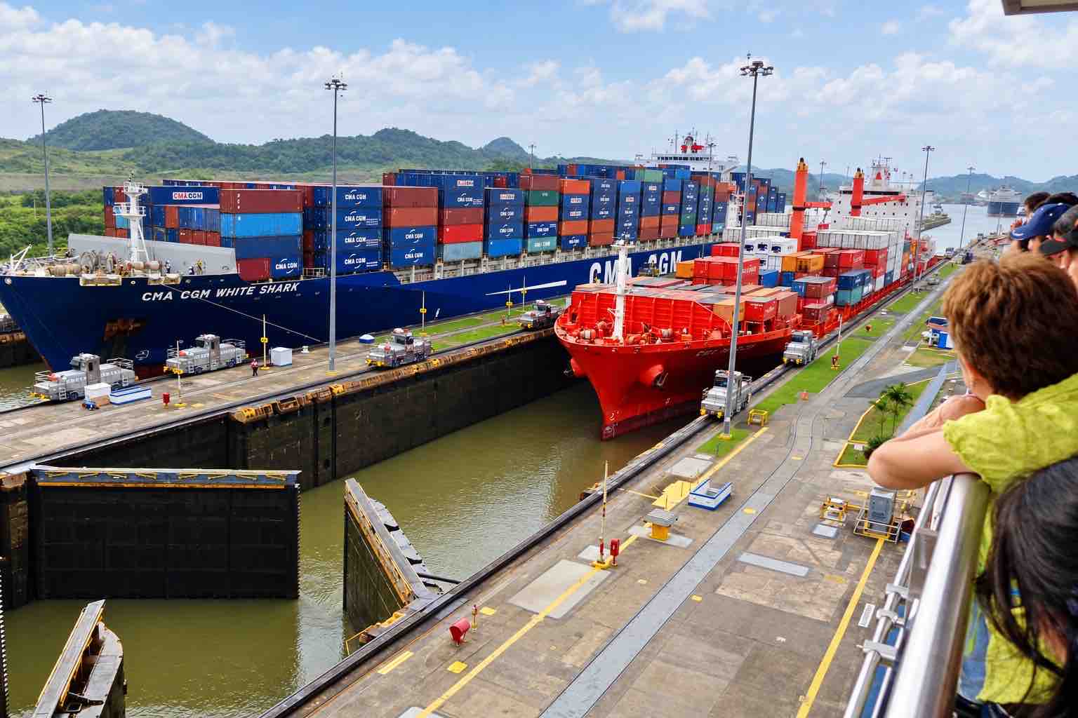 Panama Canal and City Tour: visitors watching a container ship and red tugboat at the canal locks.