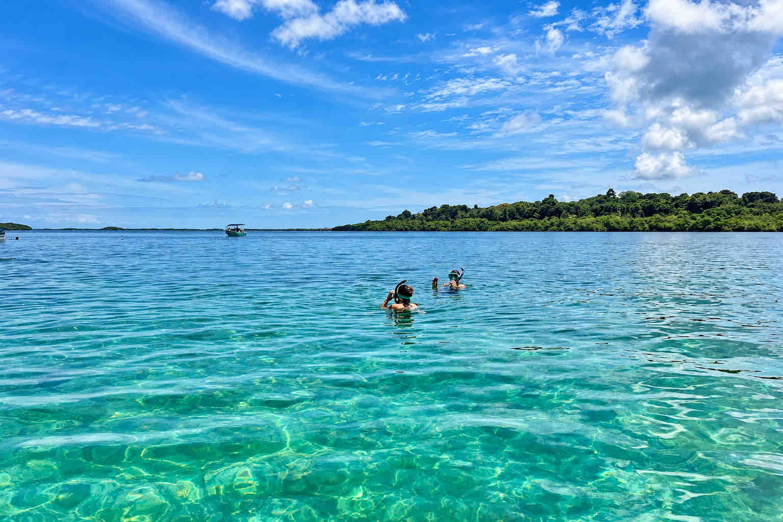 Two travelers wearing snorkel masks in calm water with forested shores behind them.