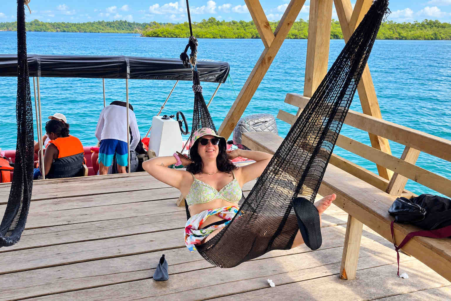 Traveler relaxing in a black hammock on a wooden waterfront deck with a boat nearby.