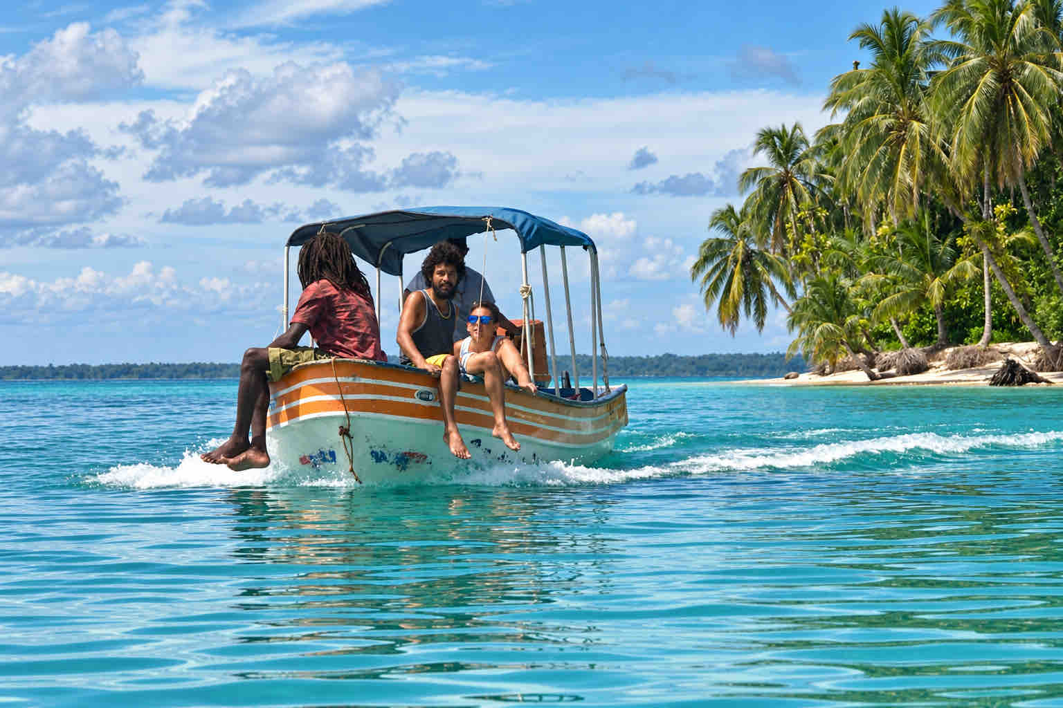 Three travelers riding in a covered motorboat beside a forest-lined beach.