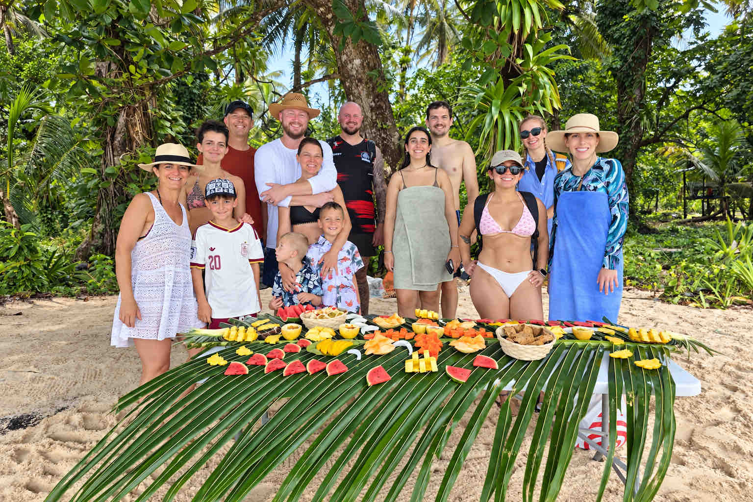 Travelers and children posing behind a tropical fruit table during a Zapatilla Island tour.