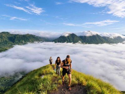 Three hikers walking along a grassy ridge above low clouds during an Anton Valley Tour