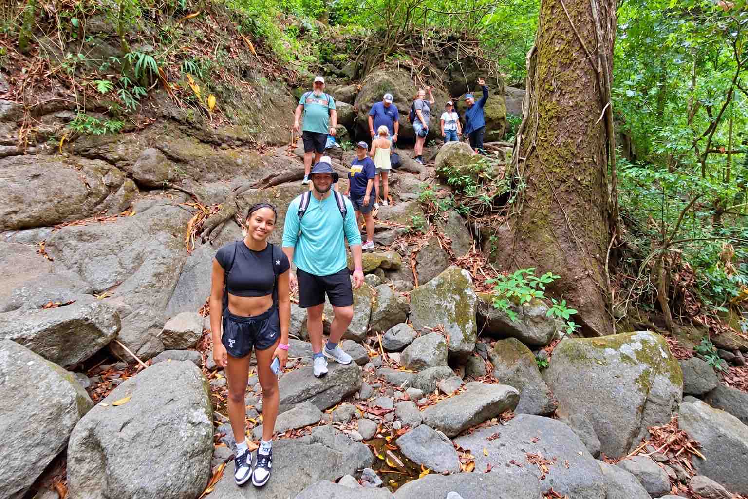 Anton Valley Tour – Hiking Group in the Forest Group of hikers on a rocky trail beside a large tree in the forest