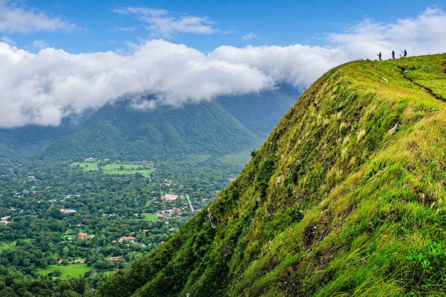 Hikers on a grassy ridge above a misty El Valle de Anton