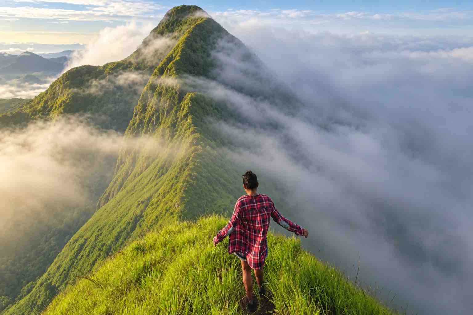 Traveler in a red checked shirt on a grassy ridge surrounded by mist