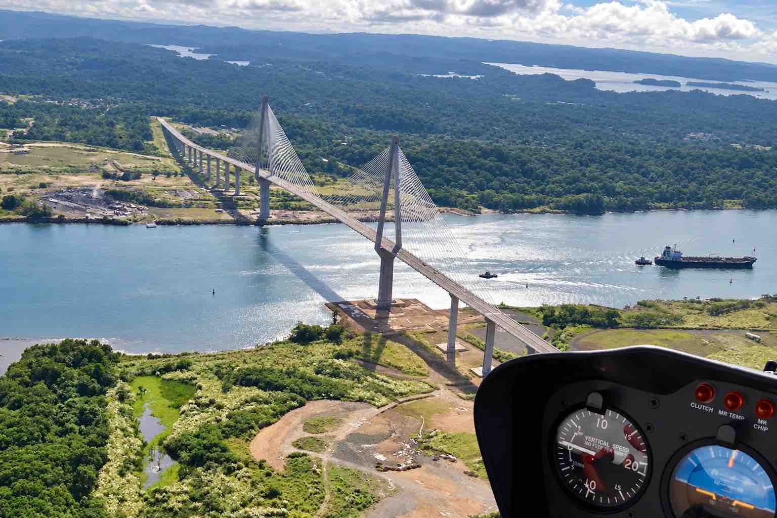 Panama Helicopter Tour – Canal Bridge Cockpit View Panama helicopter tour: Cable-stayed bridge and a ship seen through a helicopter windshield.