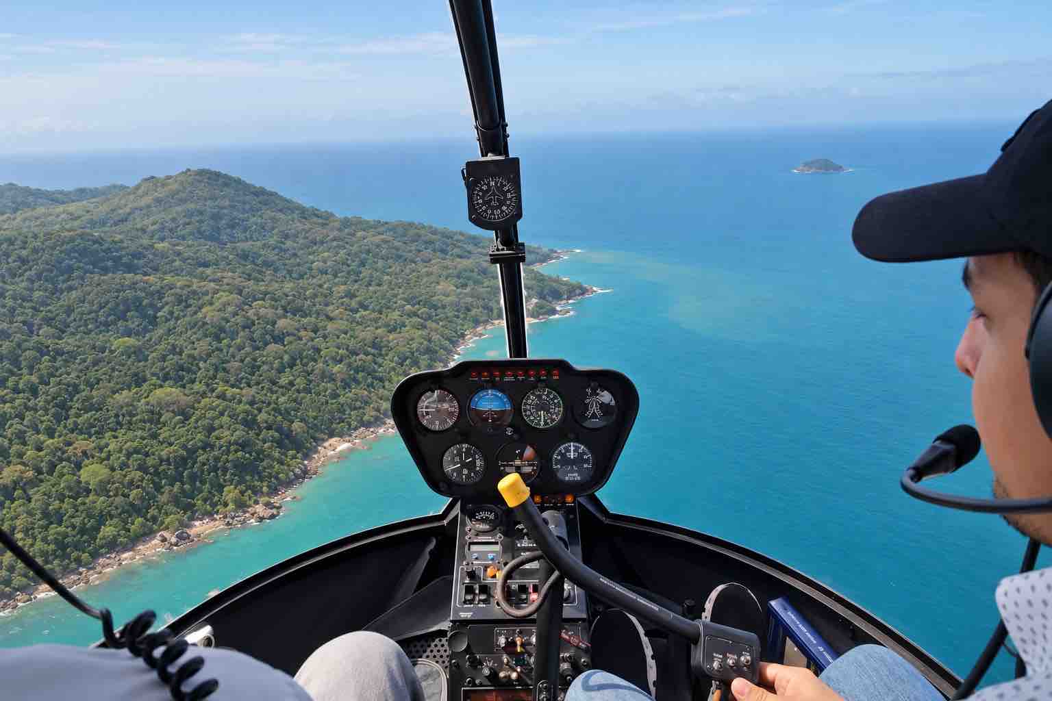 Panama helicopter tour cockpit with the pilot’s profile and a forested Taboga island coastline beside turquoise water.