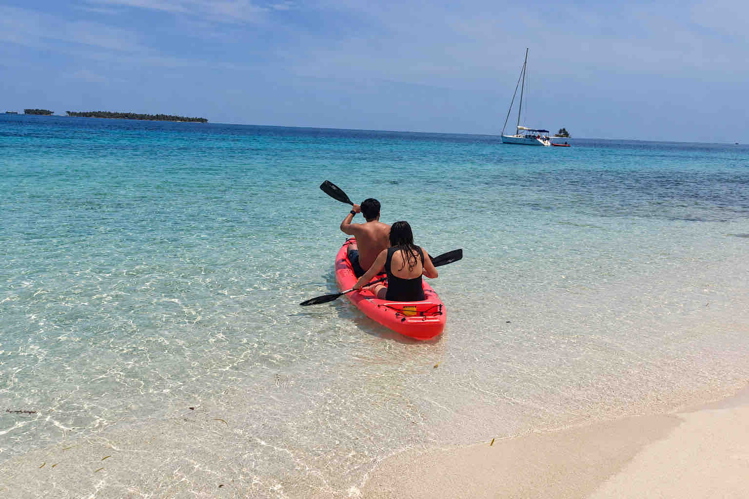 Two guests paddling a red tandem kayak in clear shallow water at Isla Perro San Blas