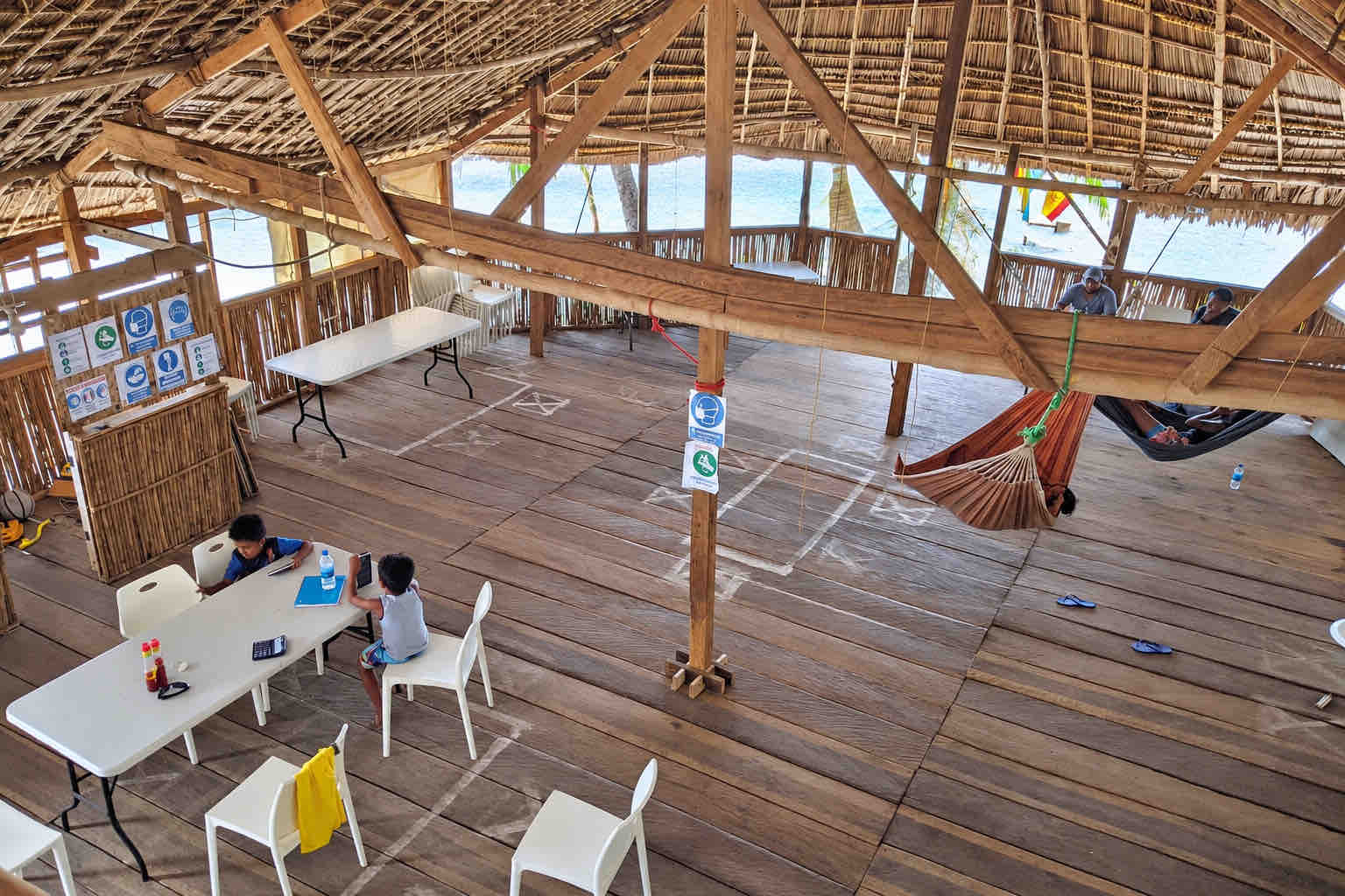Wooden main hall with tables, chairs and hammocks beneath a thatched roof at Isla Perro San Blas