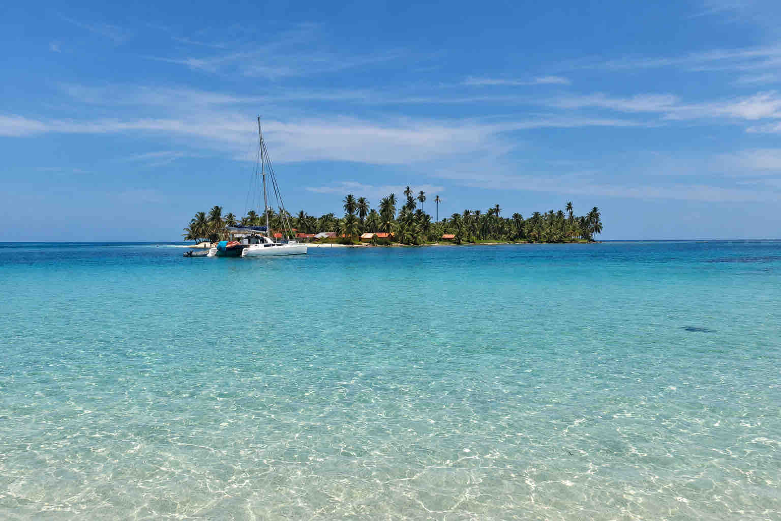 View across clear water toward Isla Diablo and an anchored catamaran at Isla Perro San Blas