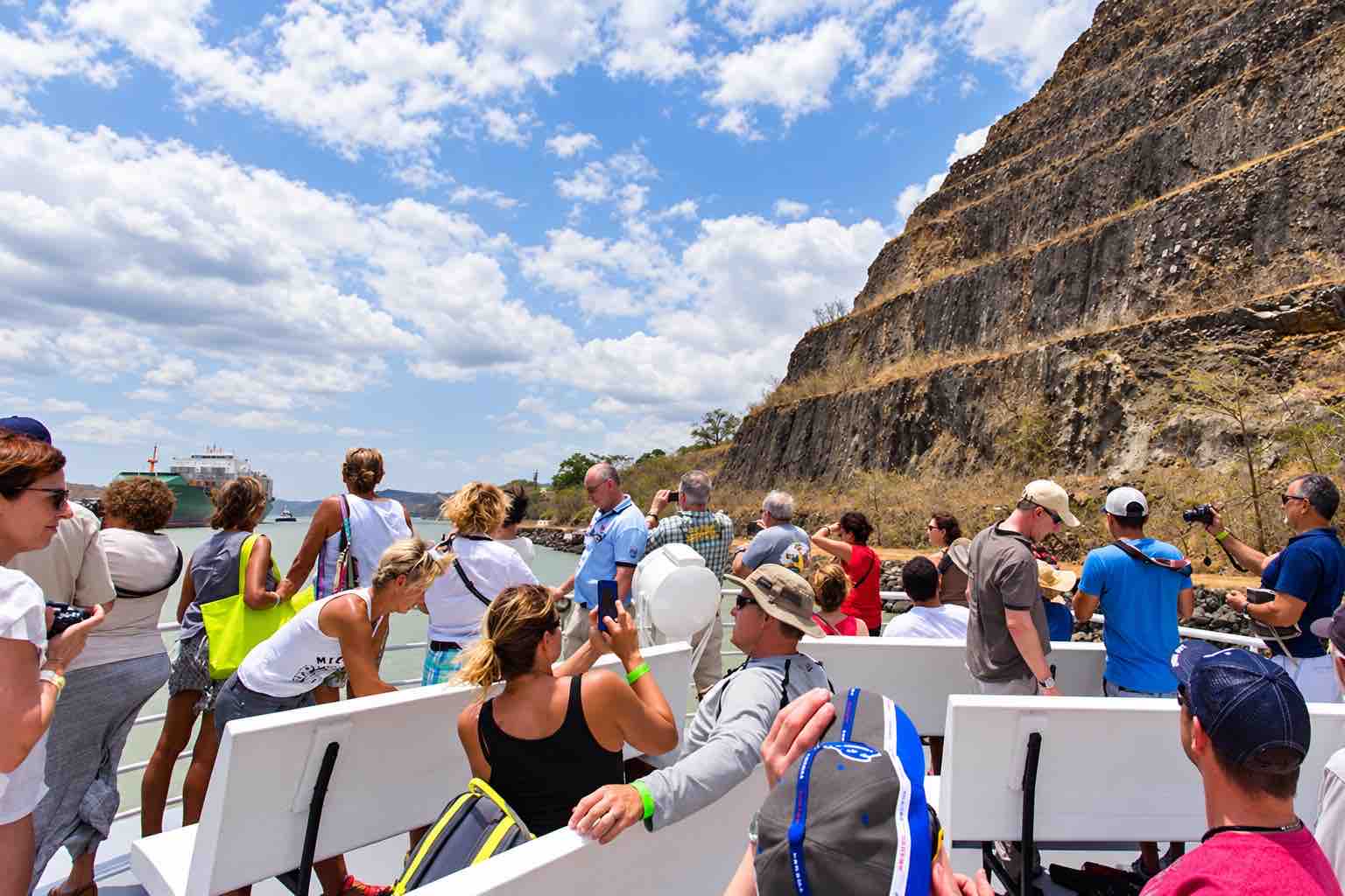 Panama Canal Partial Transit Tour – Pacific Queen Open Deck Guests Panama Canal partial transit tour: passengers on the Pacific Queen open deck beside a rocky canal cutting.