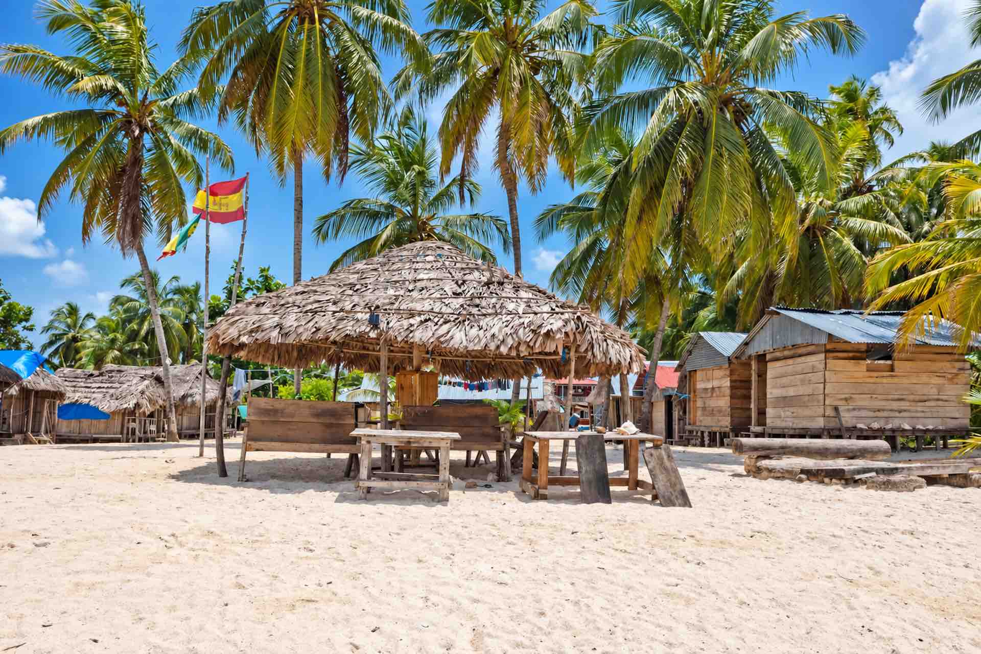 Thatched beach gazebo with tables and chairs beneath palms on Isla Ina San Blas