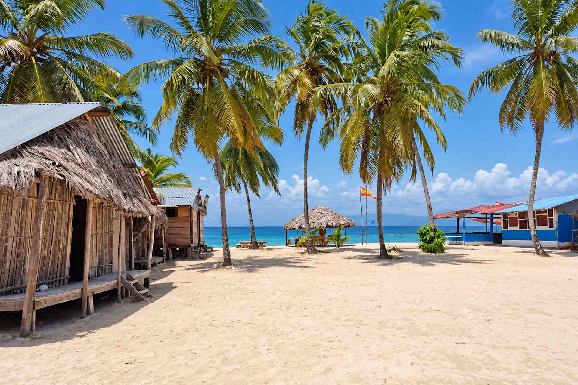 Rustic cabins under palm trees beside the sandy beach on Isla Ina San Blas