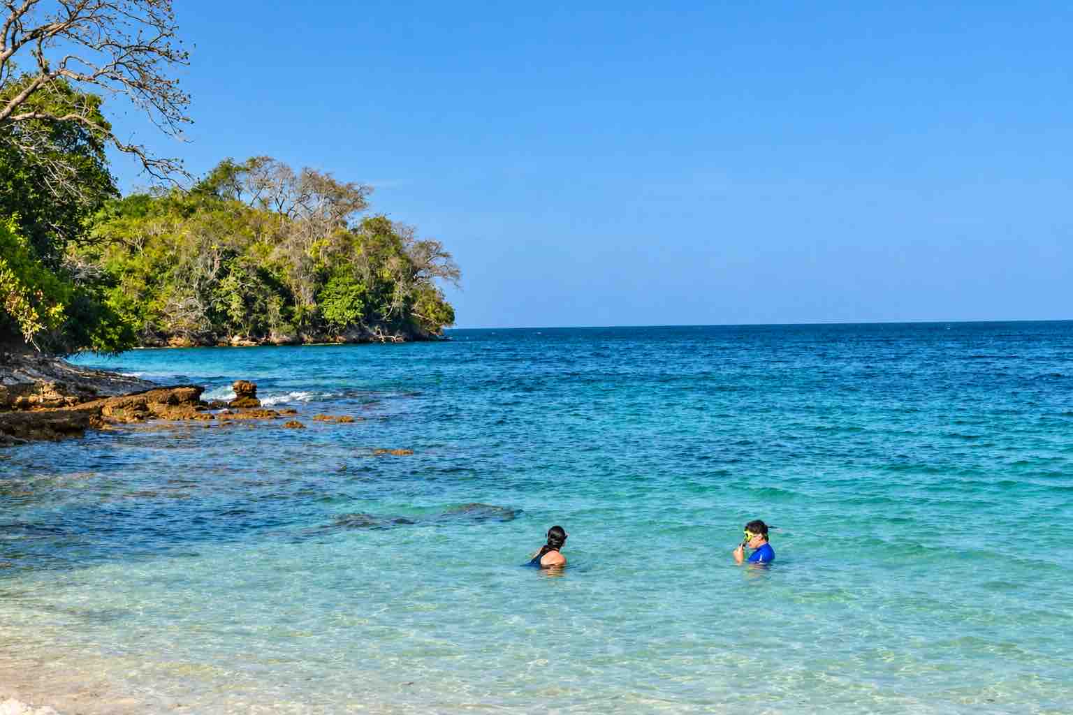 Guests with snorkeling equipment near a rocky shore during a Pearl Islands Panama Day Trip