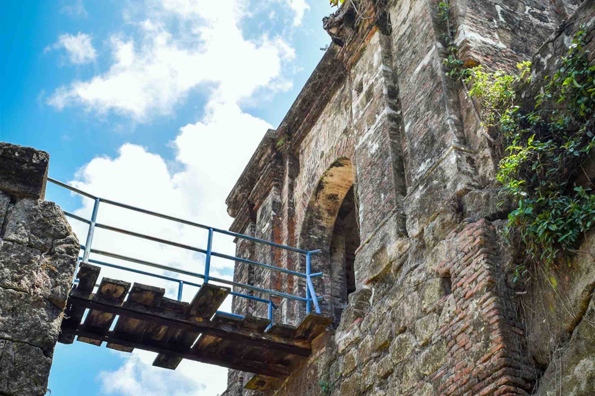 Wooden bridge with blue railings leading to a stone arch at Fort San Lorenzo on the Ocean to Ocean Panama Canal Tour