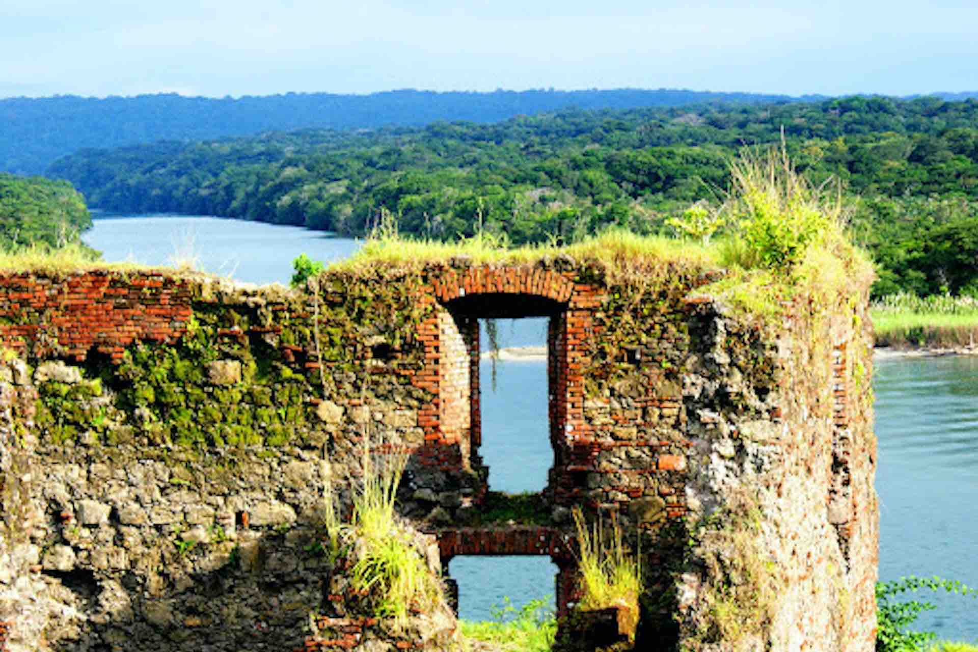 Weathered stone wall and opening at Fort San Lorenzo with water and forest beyond on the Ocean to Ocean Panama Canal Tour