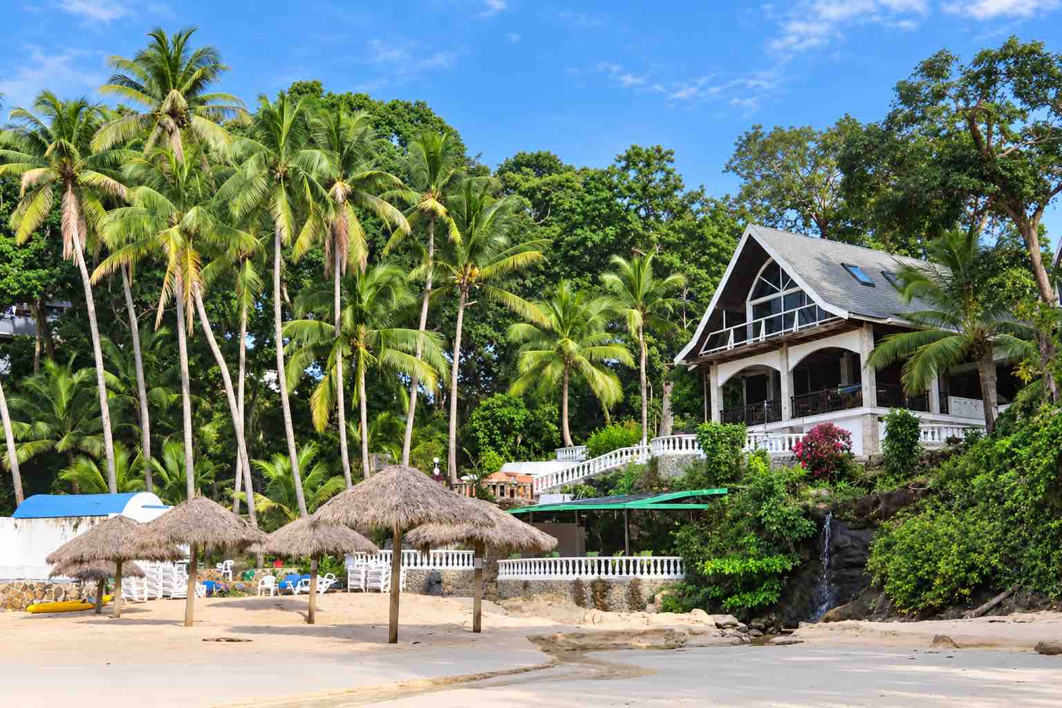 Mar y Oro Contadora – Hotel exterior surrounded by palms above the sand and thatched umbrellas