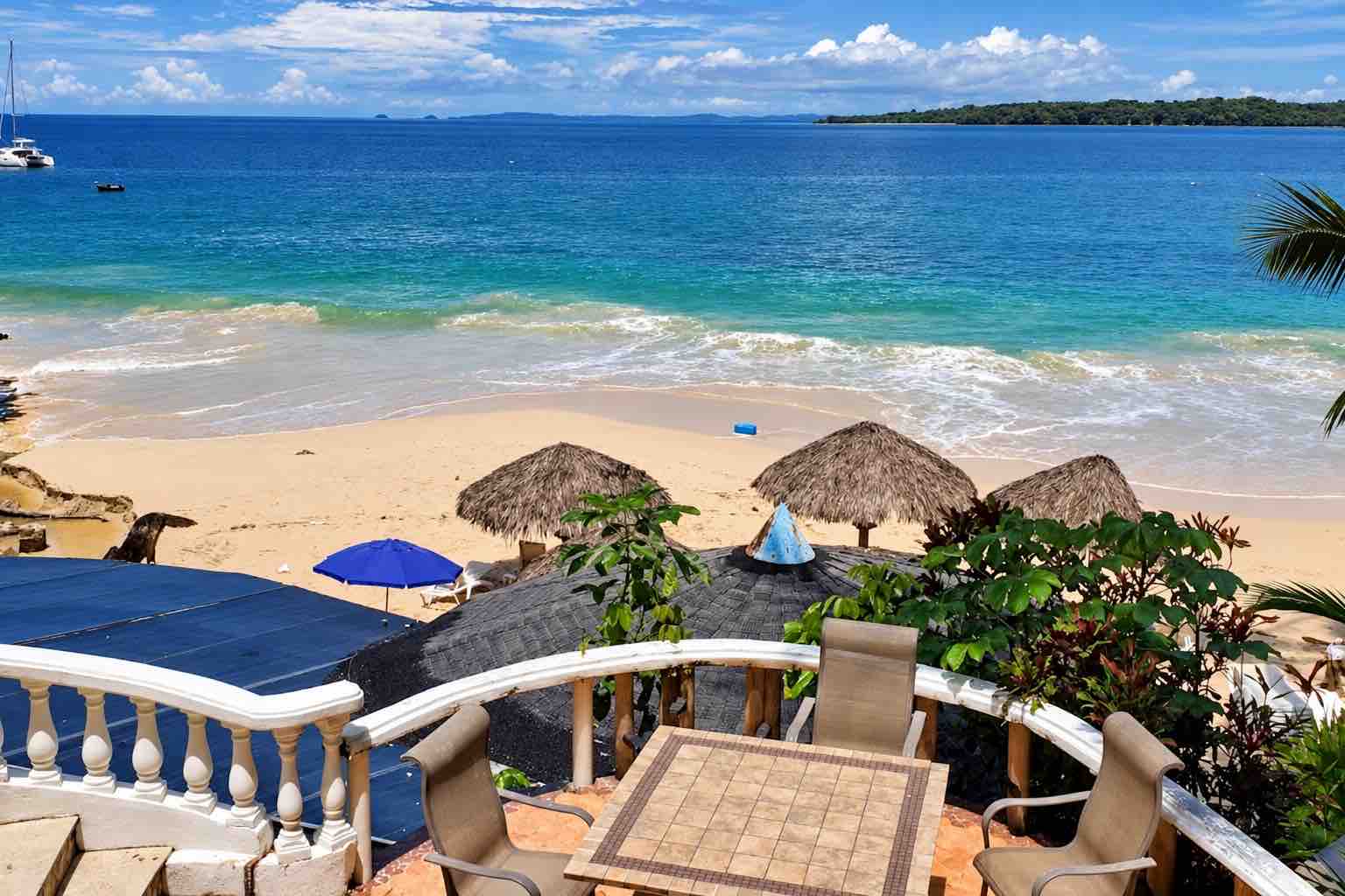 Mar y Oro Contadora – Terrace table and chairs overlooking thatched beach umbrellas and blue sea