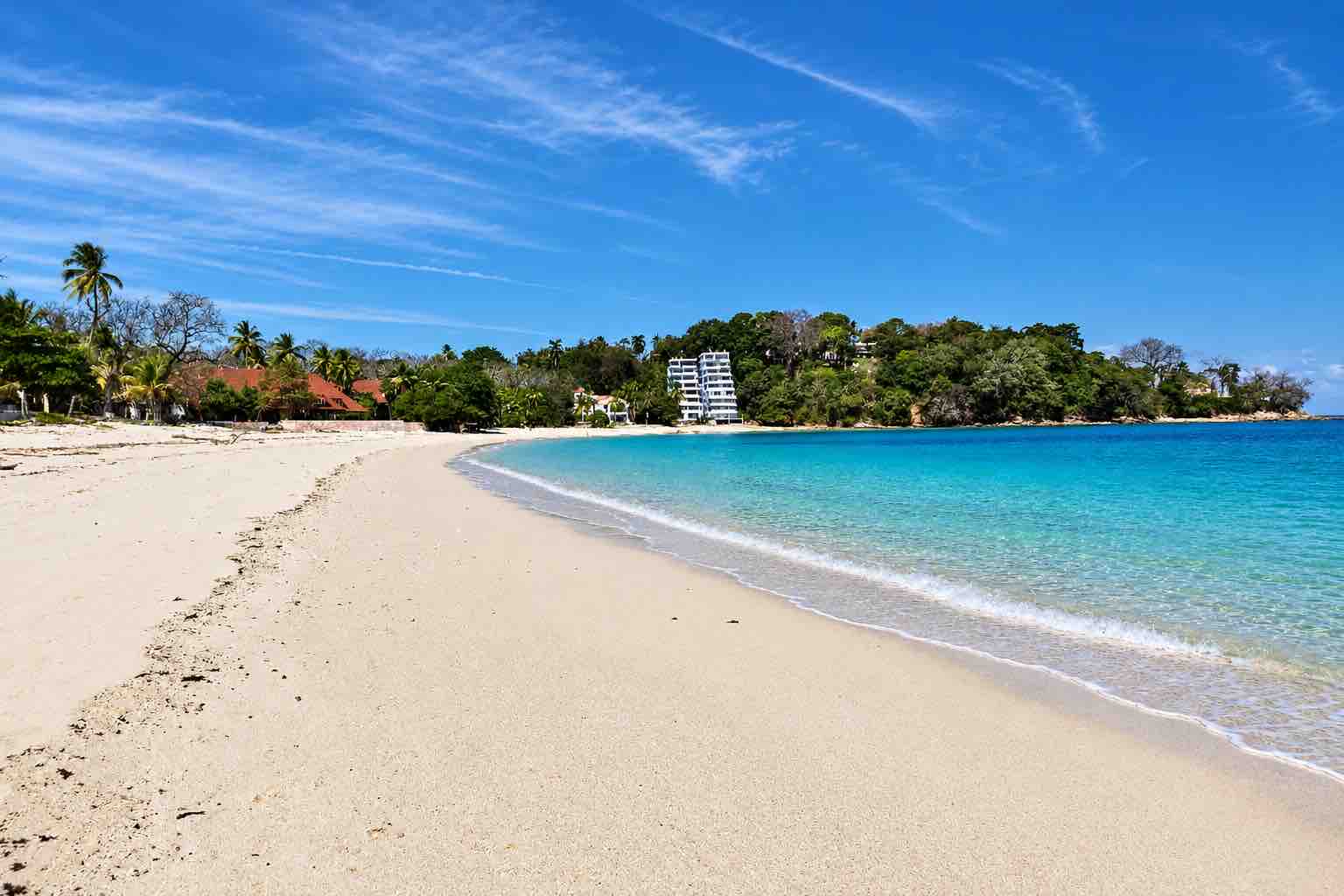 Pimienta y Sal – Sandy beach curving beside turquoise water and buildings at Playa Larga