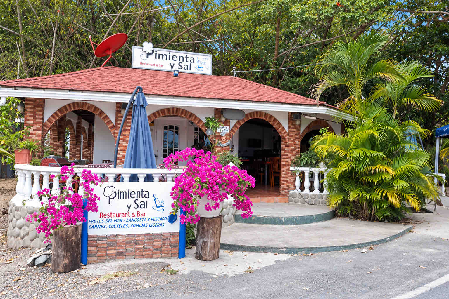 Restaurant entrance with brick arches, red roof and pink flowers at Pimienta y Sal