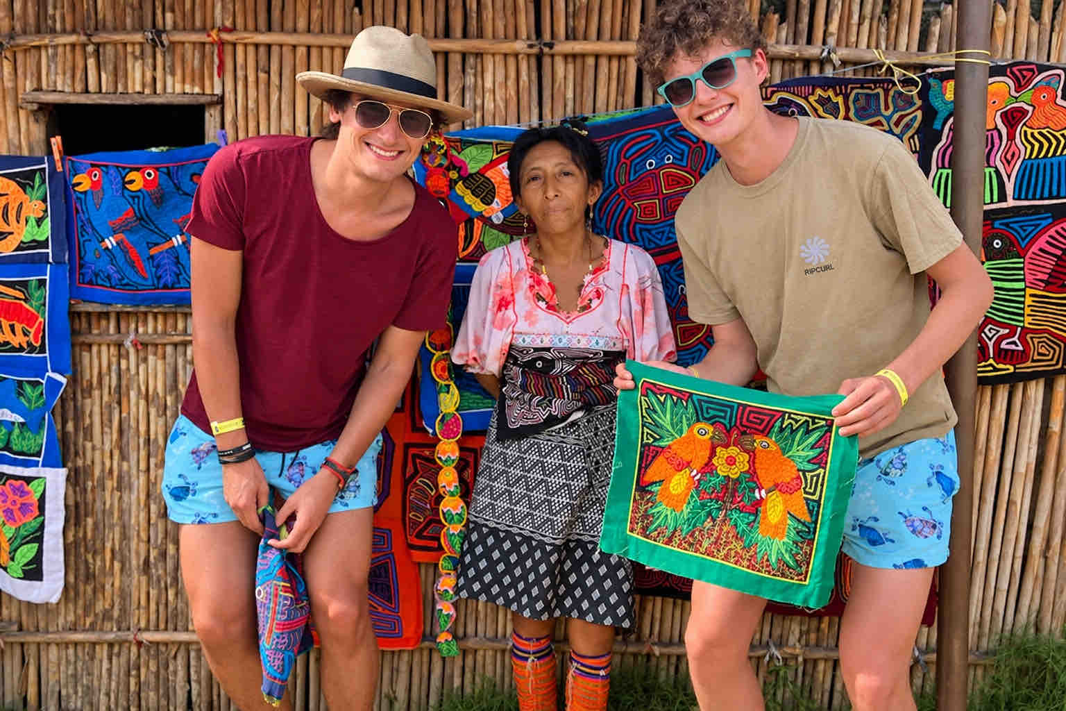 Two tour guests pose with a Guna host and a colorful mola textile