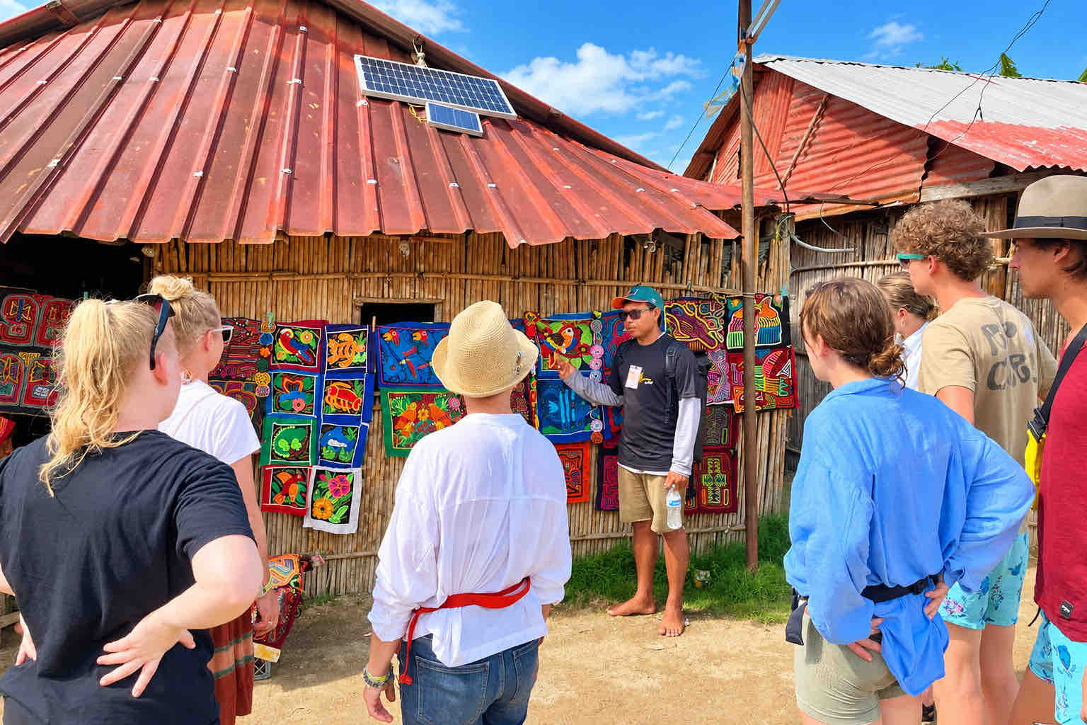 Guna Yala Tour – Mola Textile Display Local guide speaking with visitors beside colorful mola textiles in a Guna village
