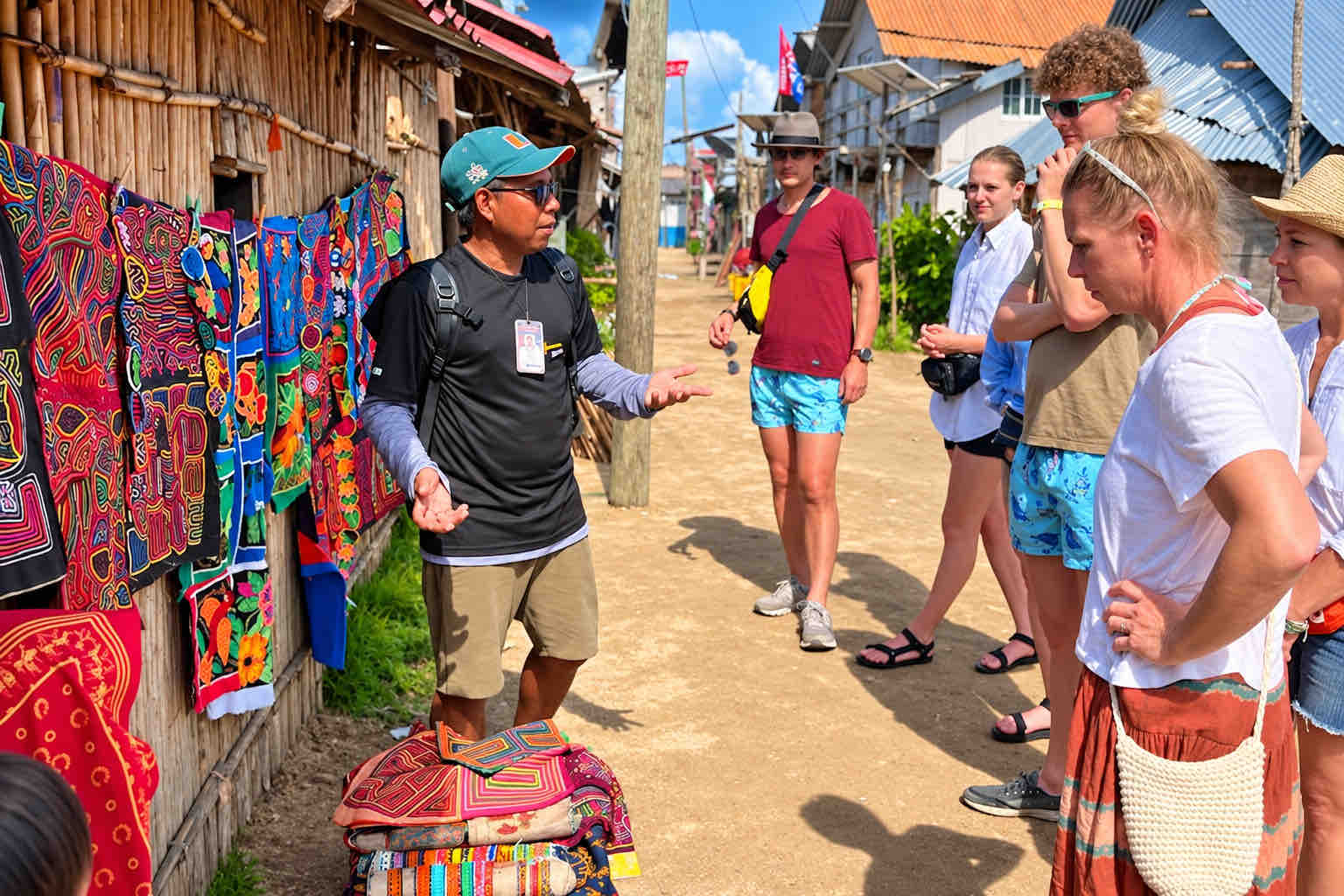 Colorful mola textiles hanging beside a village walkway as a guide speaks to guests