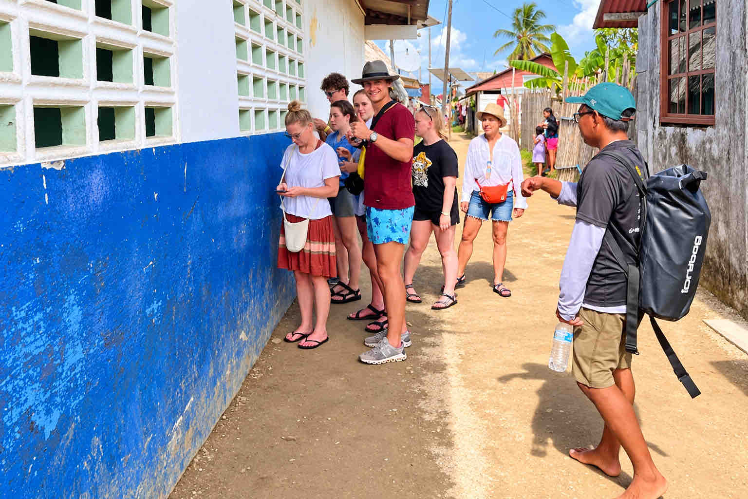 Tour guests walking through a narrow lane between community buildings