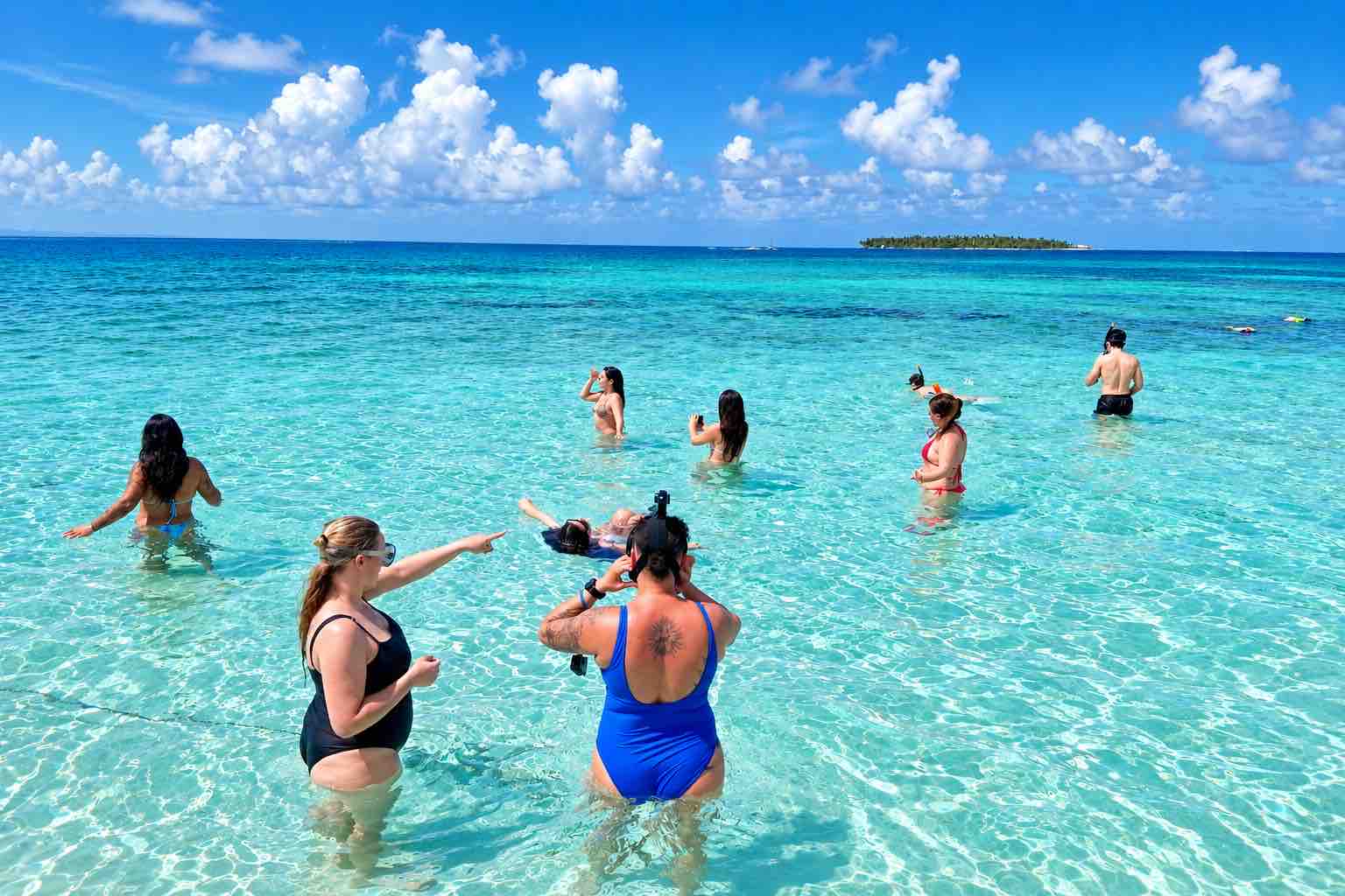 Tour guests wading in clear shallow water at the San Blas Natural Pool with an island on the horizon