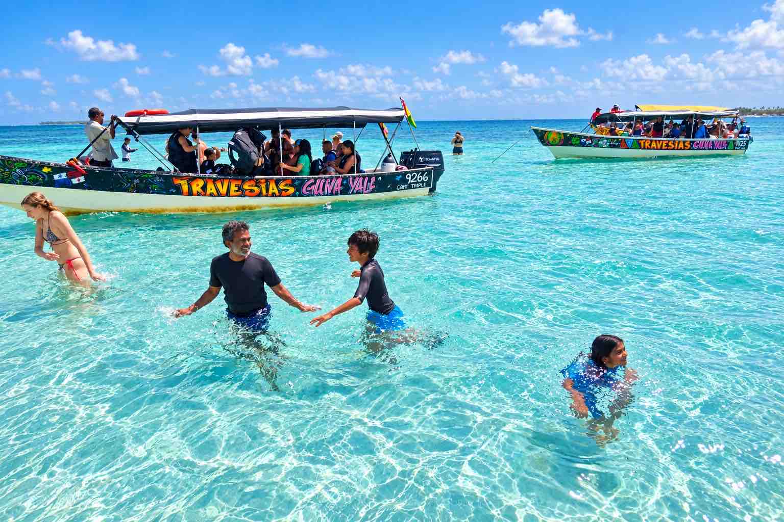 Guests standing in shallow turquoise water near two tour boats at the San Blas Natural Pool